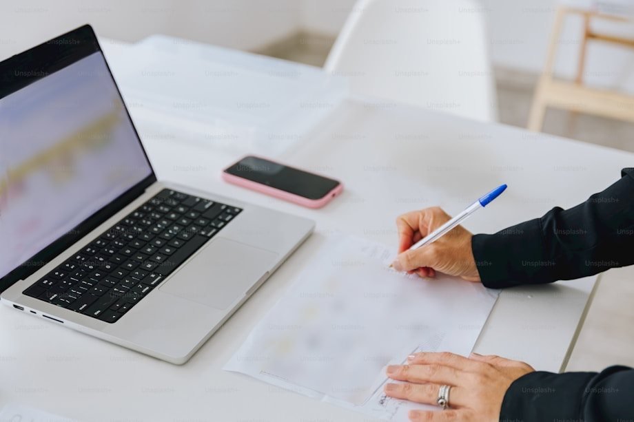 A person taking notes next to a laptop and a smartphone